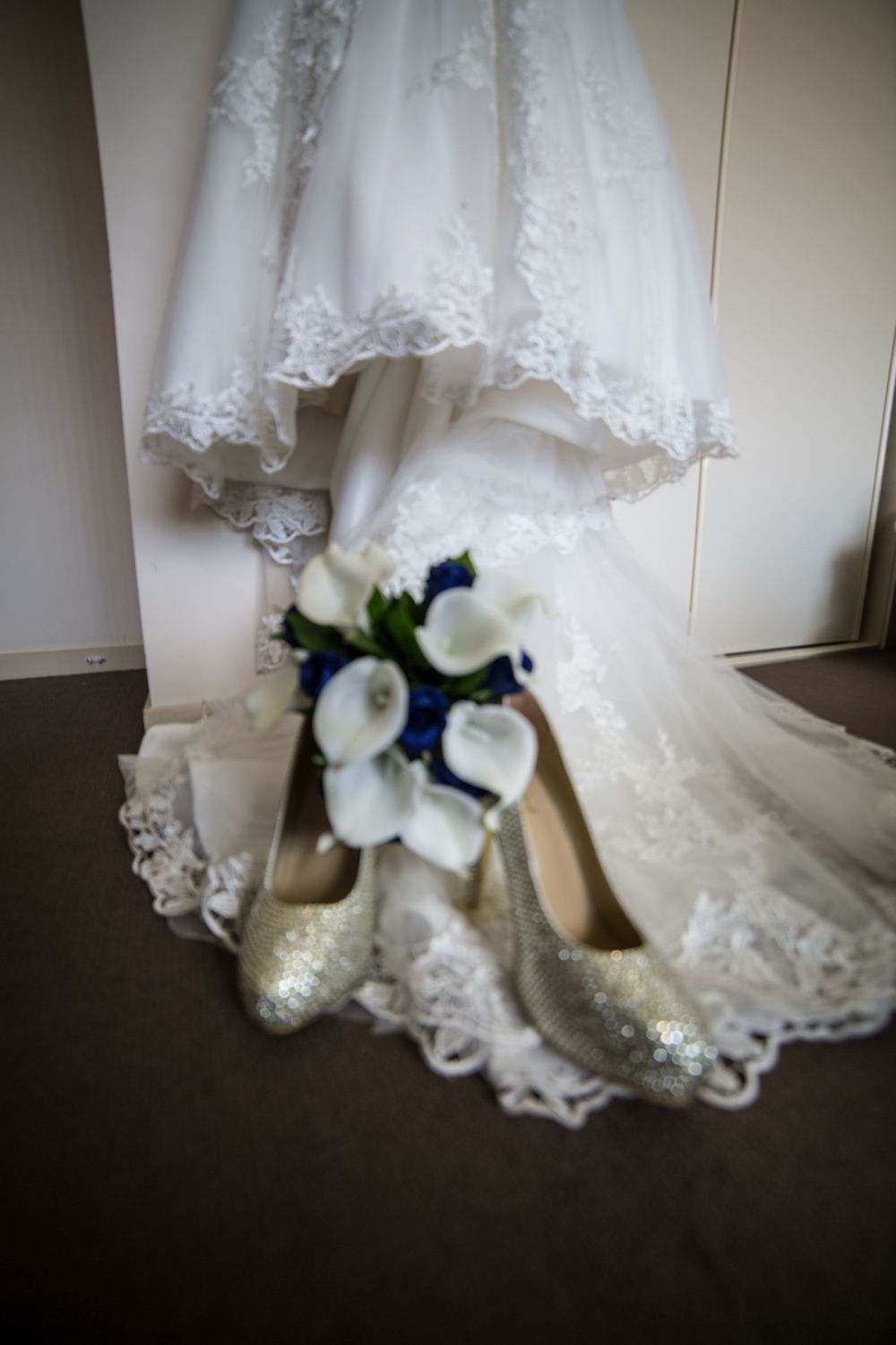 Bottom of white lace wedding dress with white floral bouquet on dark floor.
