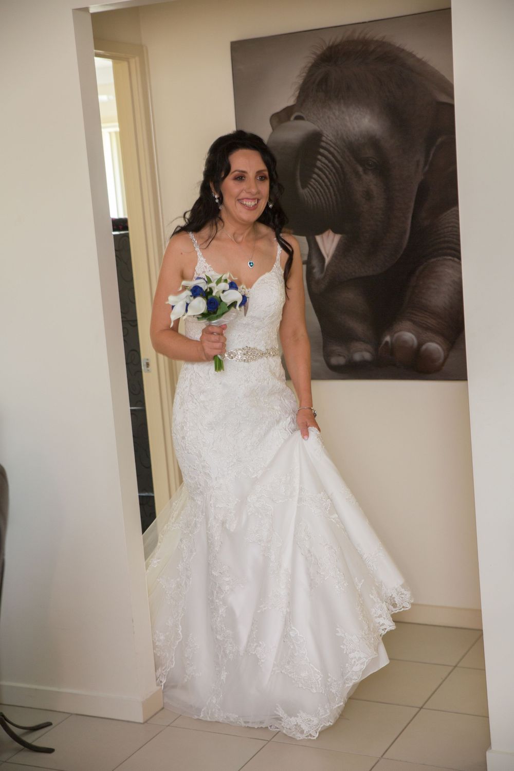 Woman in white lace wedding dress standing and smiling in room.
