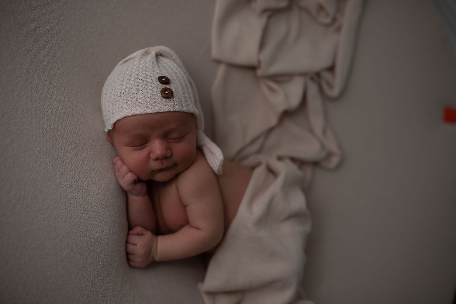 Sleeping newborn wearing white knit hat against neutral backdrop.