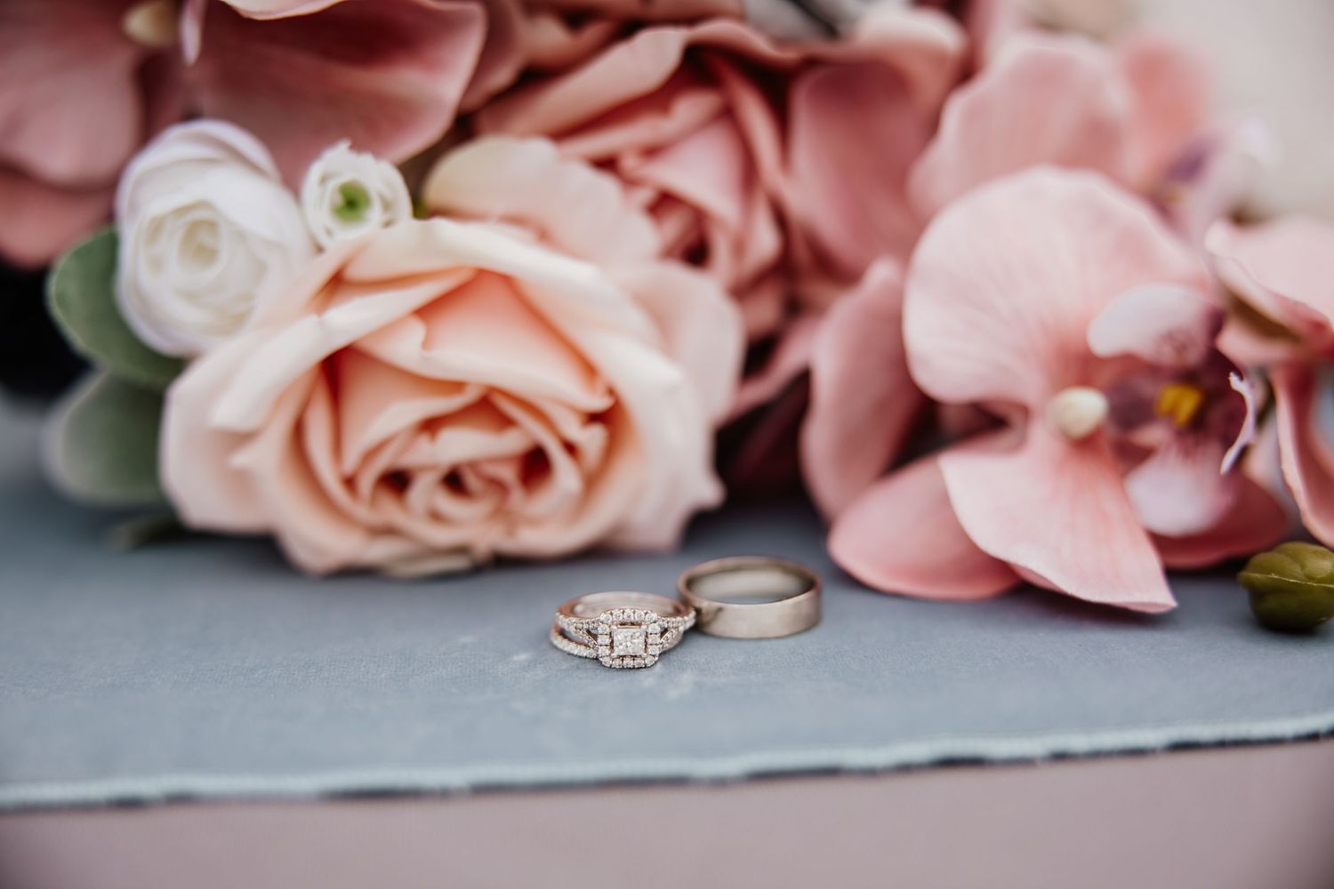 Wedding rings displayed with pink and peach roses on gray paper.
