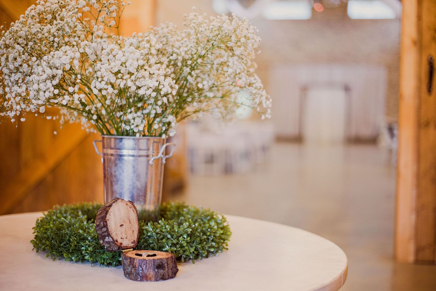 Baby's breath flowers in a metal vase with wooden decor pieces on a white table.