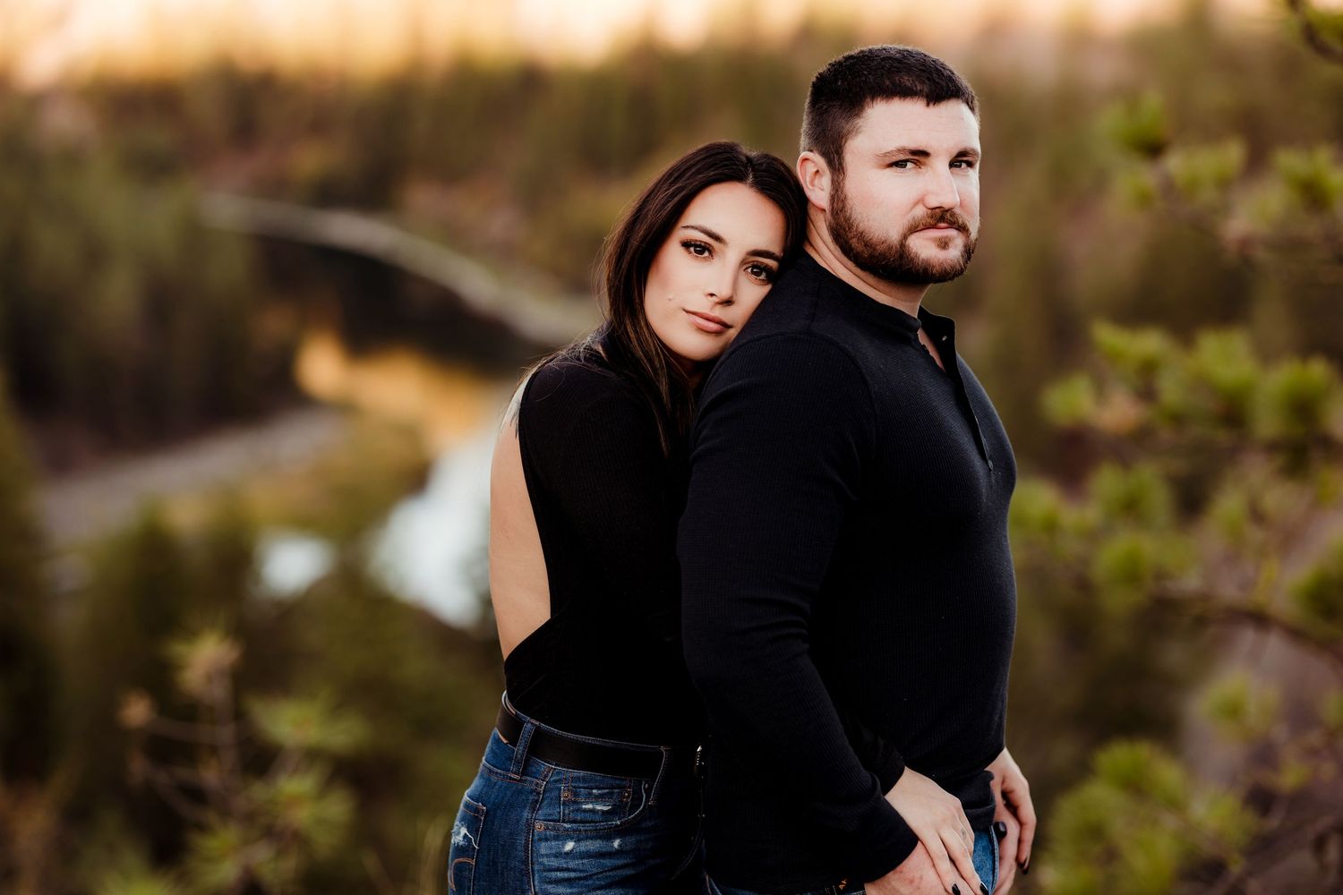 A couple in matching black outfits posing against a scenic mountain backdrop at sunset.