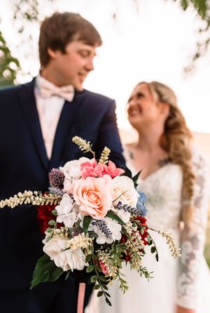 A joyful wedding couple shares a laugh while holding a beautiful pink and white floral bouquet.