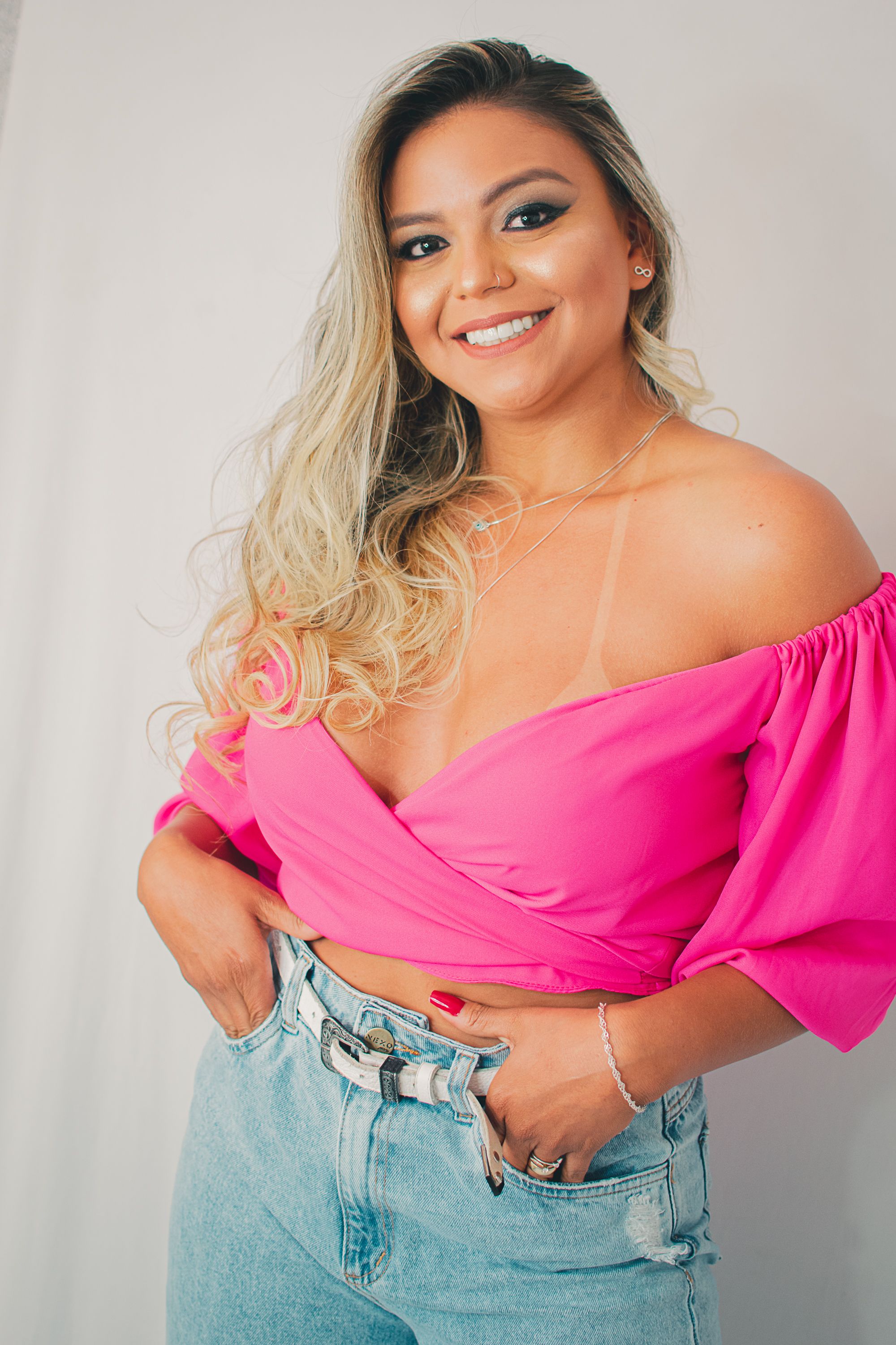 Stylish portrait in bright pink off-shoulder top and light denim jeans against white background.