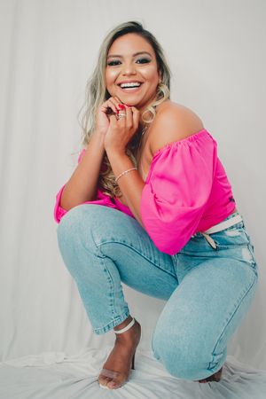 Playful fashion poses in pink crop top and blue jeans against white backdrop.