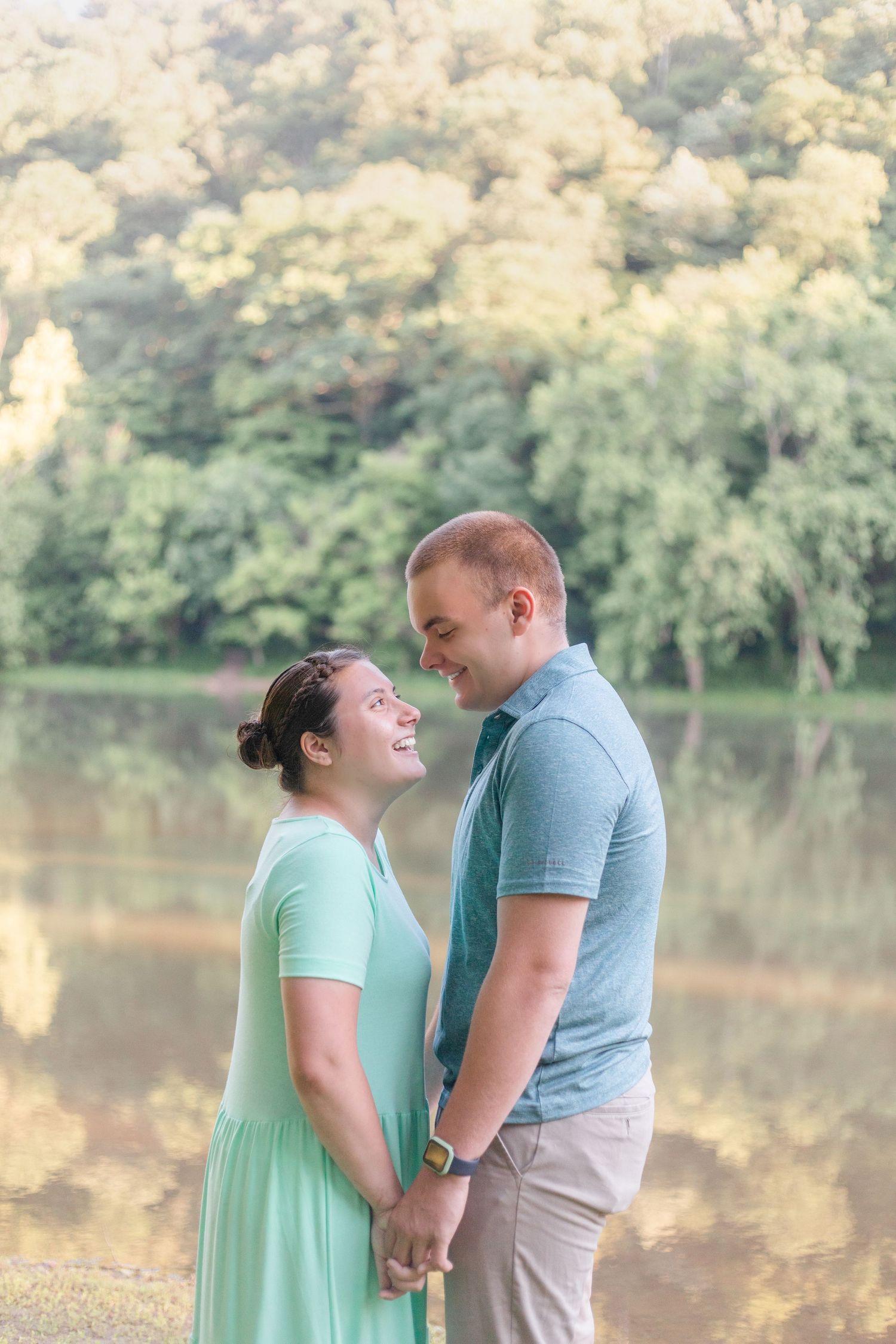 Two people in coordinating mint and gray outfits share a laugh by a serene lake at sunset.