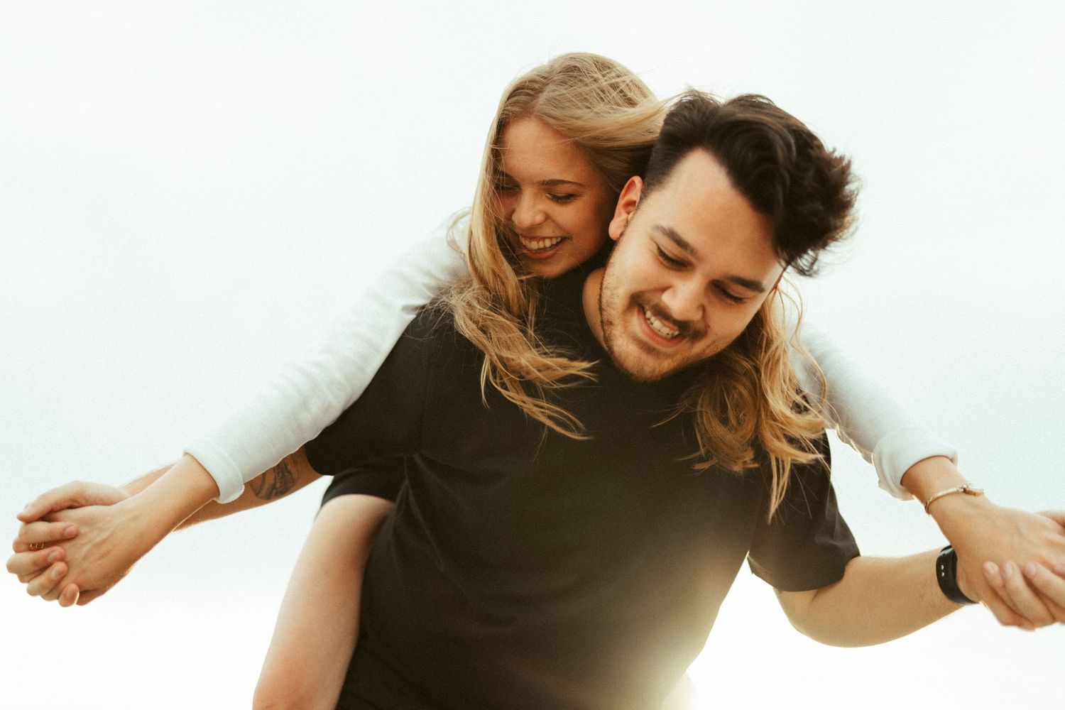 Joyful couple spinning and embracing against bright sky background.