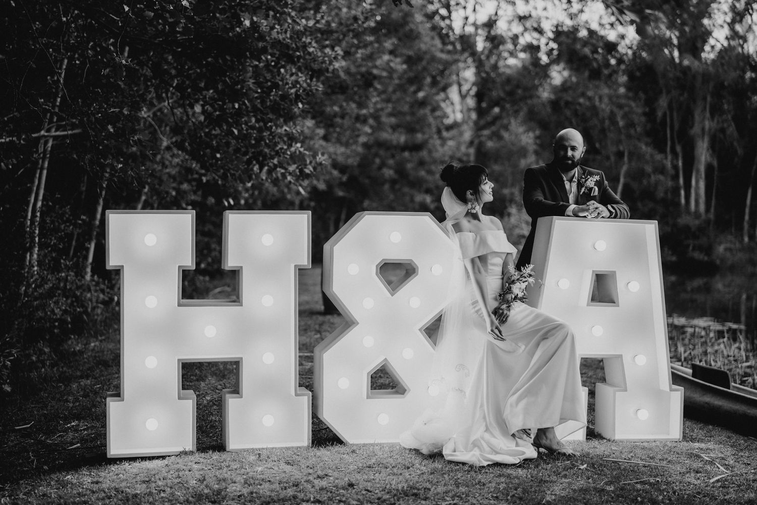 Black and white photo of a couple sitting by illuminated H&A marquee letters outdoors.