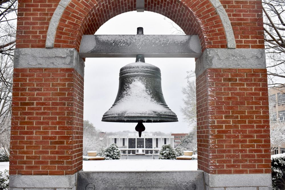 Historic bell framed by brick archway on a snowy winter day.
