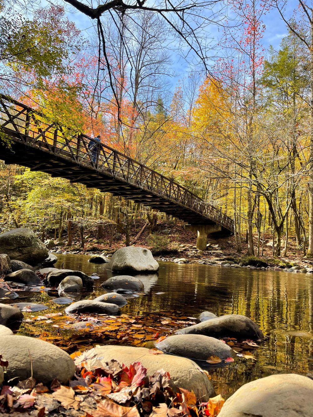 Rustic footbridge spans a rocky stream surrounded by colorful fall foliage.