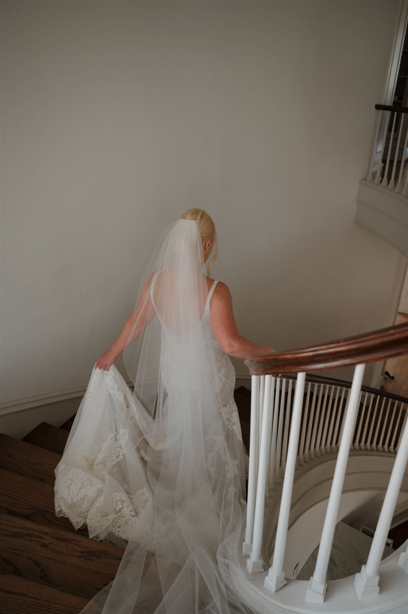 Long flowing wedding dress with cathedral veil captured from behind on wooden staircase.