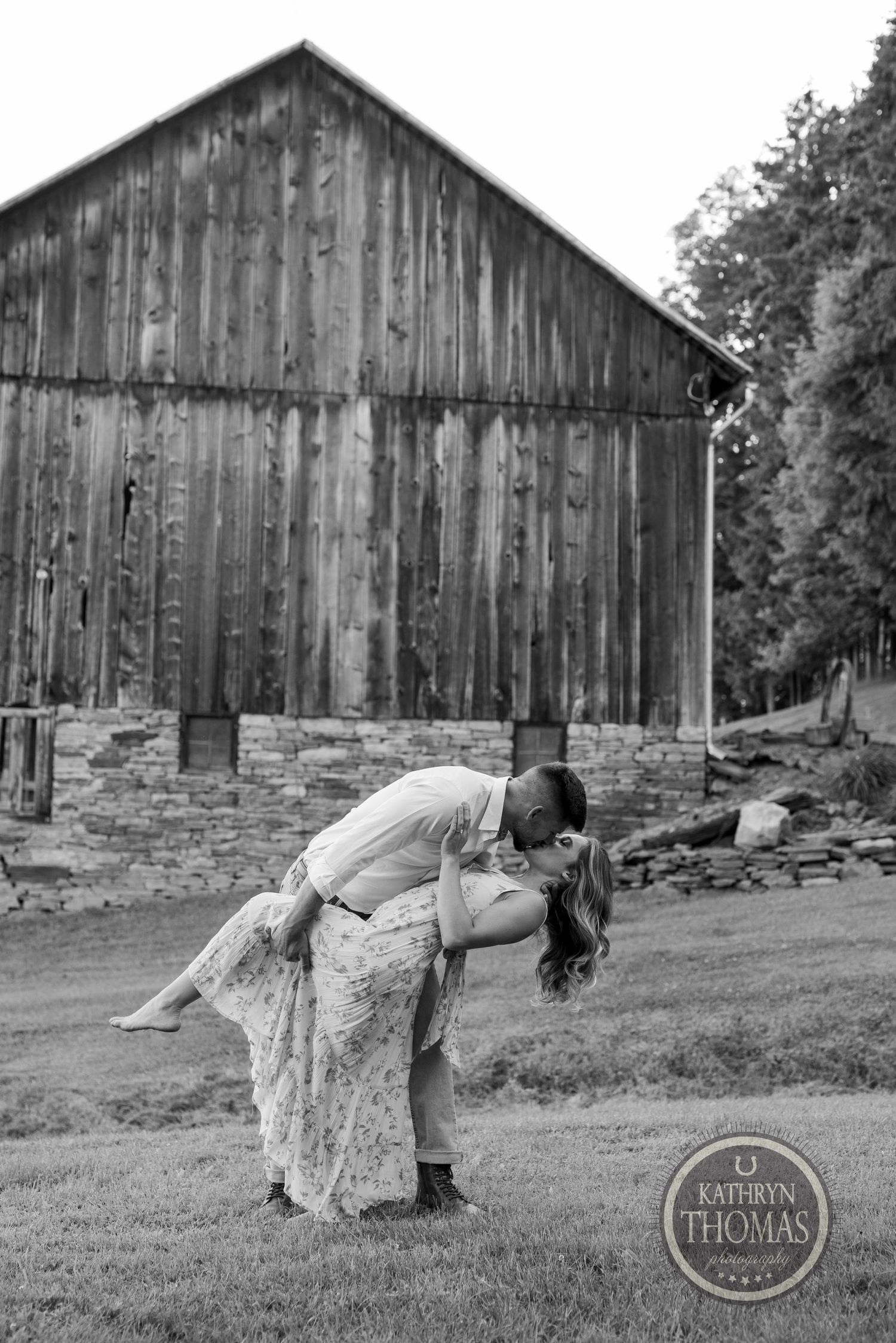 A romantic dip pose in front of a weathered barn captured in black and white.