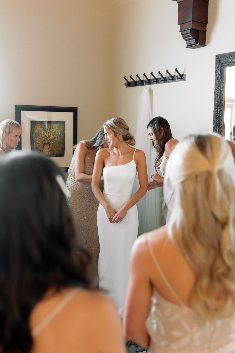 Bride in elegant white dress surrounded by wedding party during preparations.