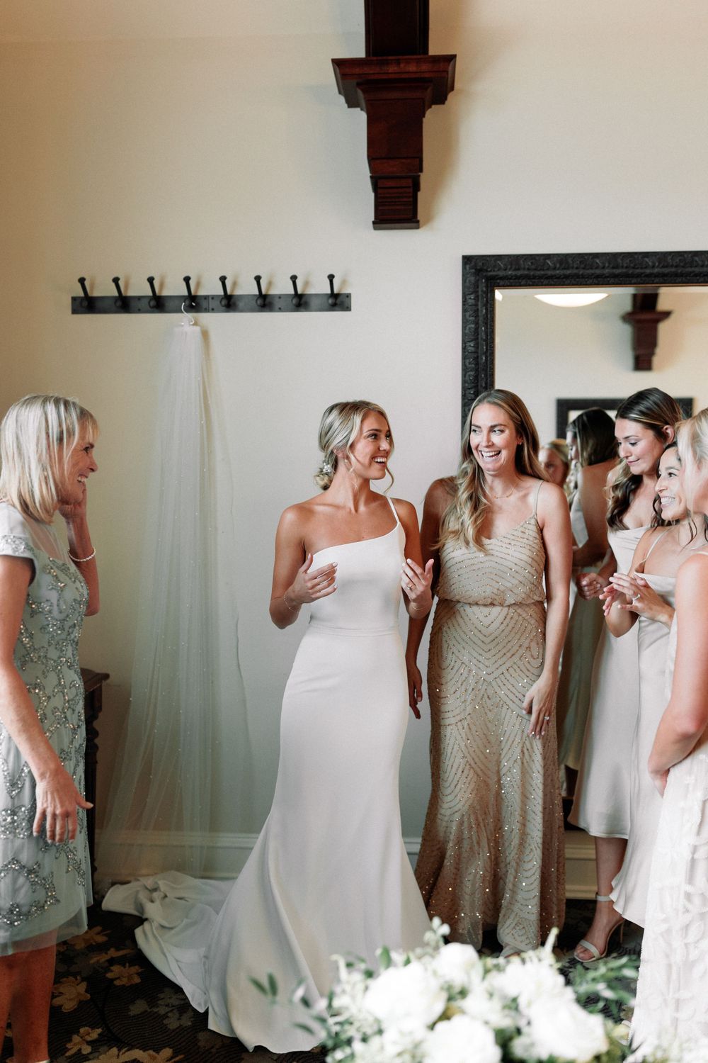 Bridal party in elegant gowns shares a joyful moment in a dressing room.
