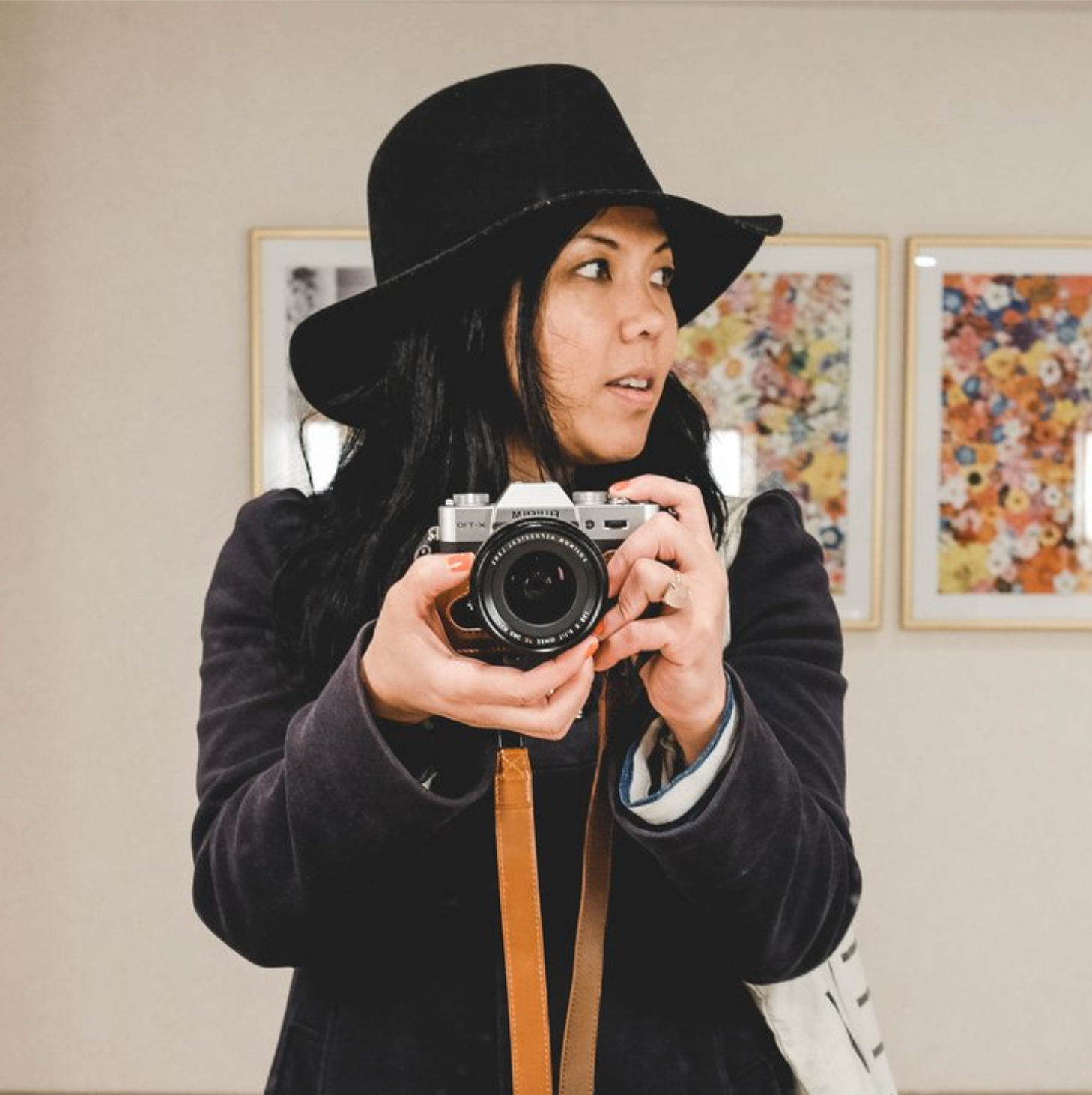 Photographer in a black hat holding a camera in an art gallery setting.