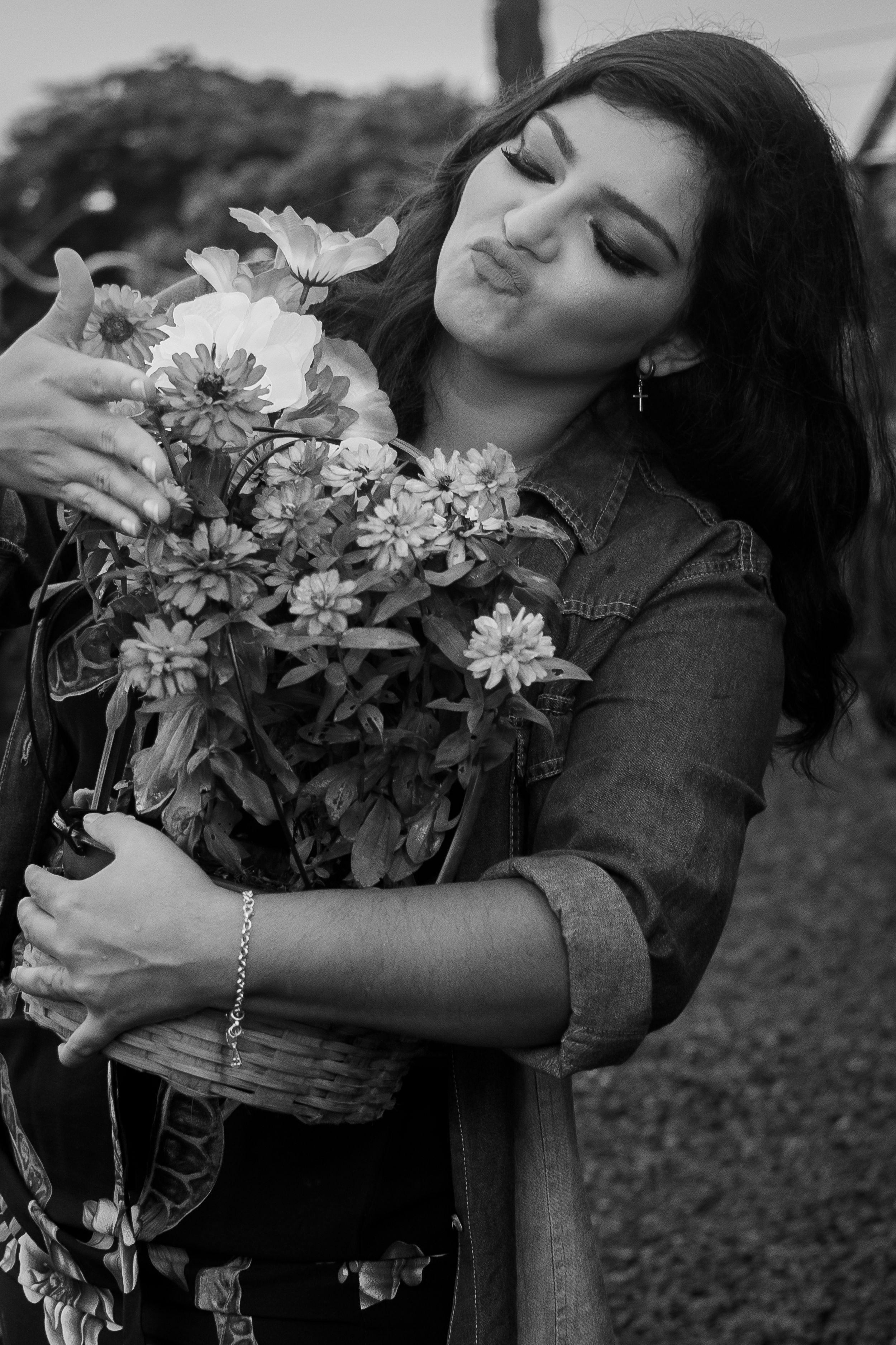 Black and white portrait of someone holding a bouquet of white flowers while wearing a denim jacket in a garden setting.