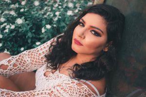 Romantic portrait of someone in a white lace garment with dark waves against greenery.