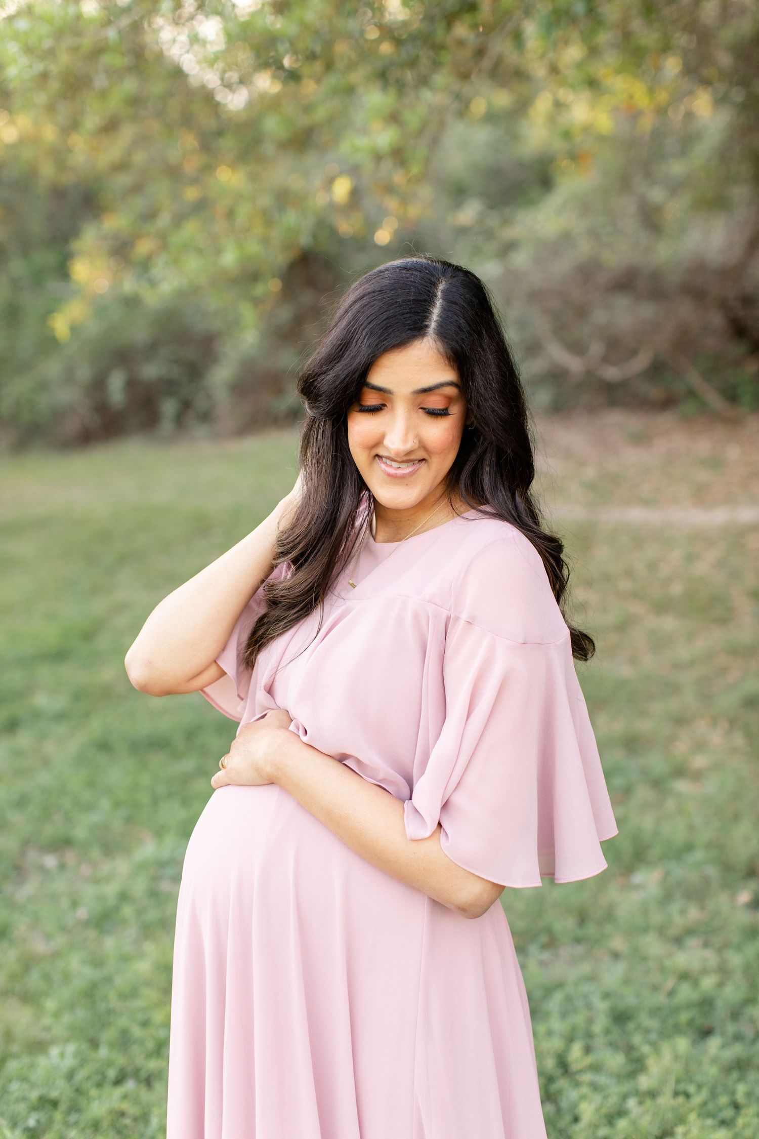 A delicate pink flutter-sleeve maternity gown creates an ethereal outdoor portrait.