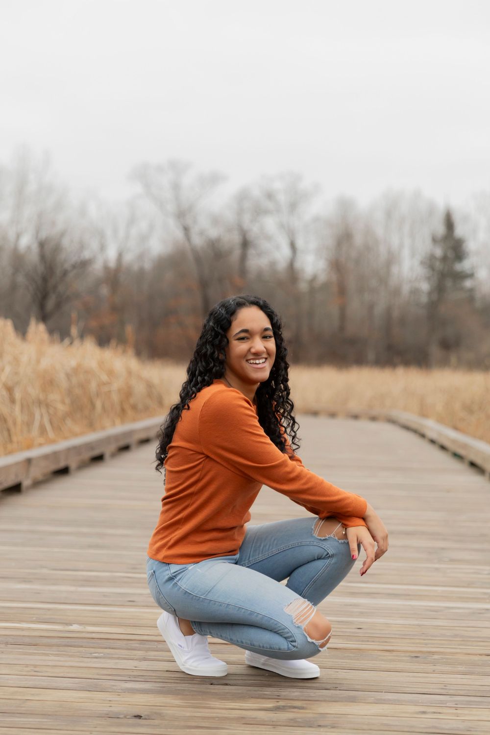 teenage girl sitting on a wooden walkway in the wintertime at innovation hills park in Rochester hills