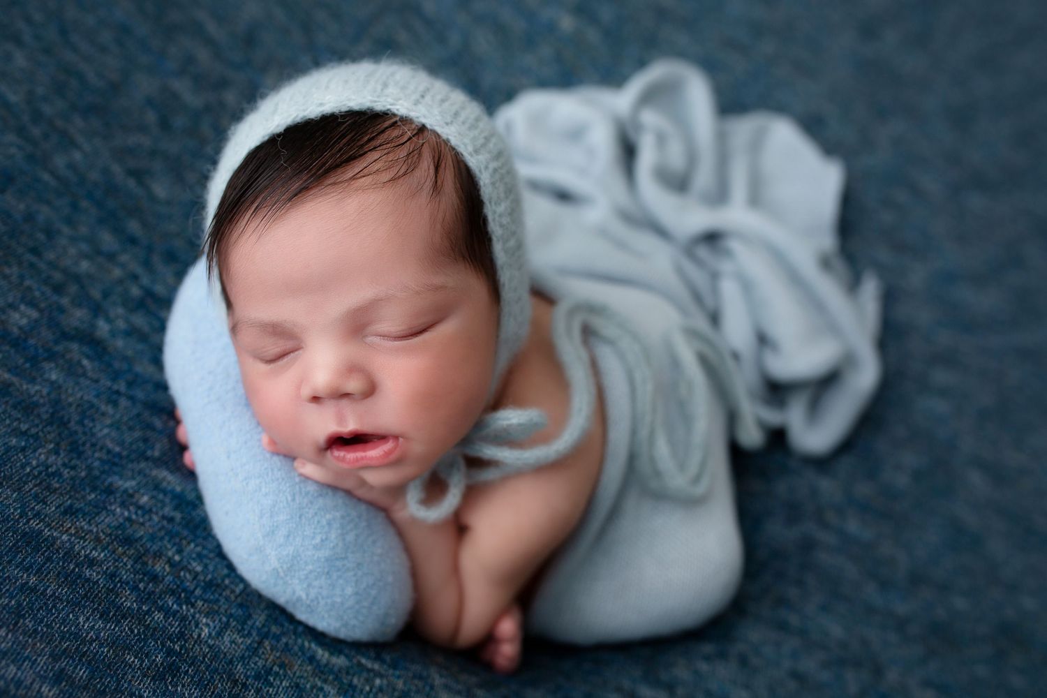 A peaceful sleeping newborn wrapped in soft blue swaddle on dark fabric.