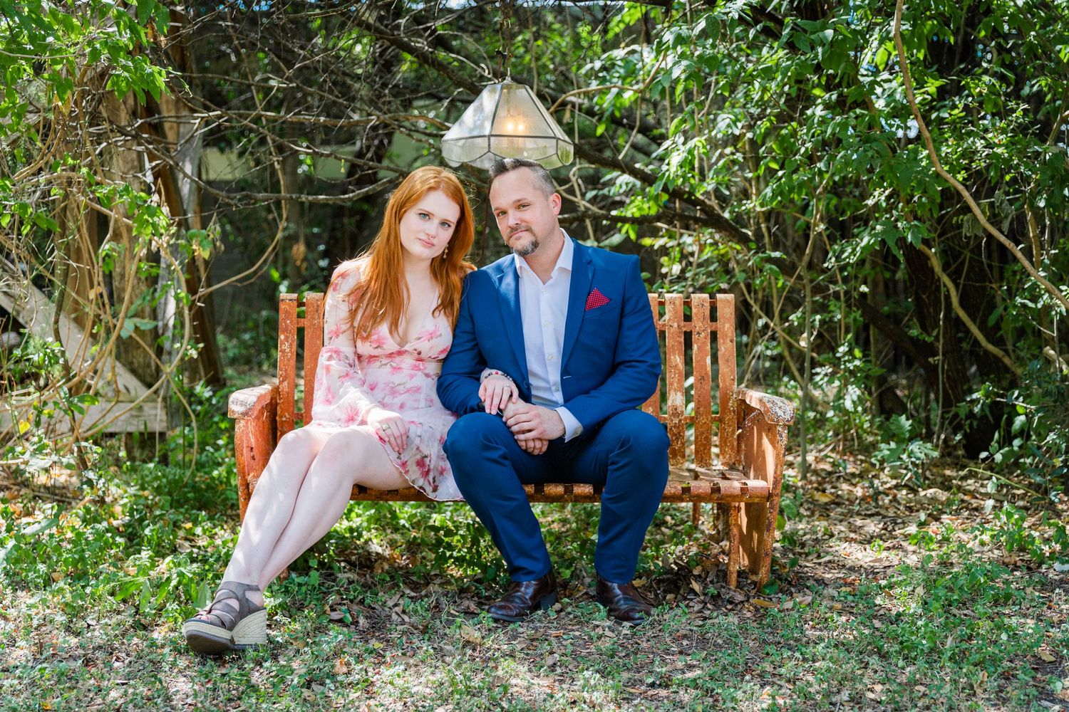 couple sitting on rustic bench under tree lanterns