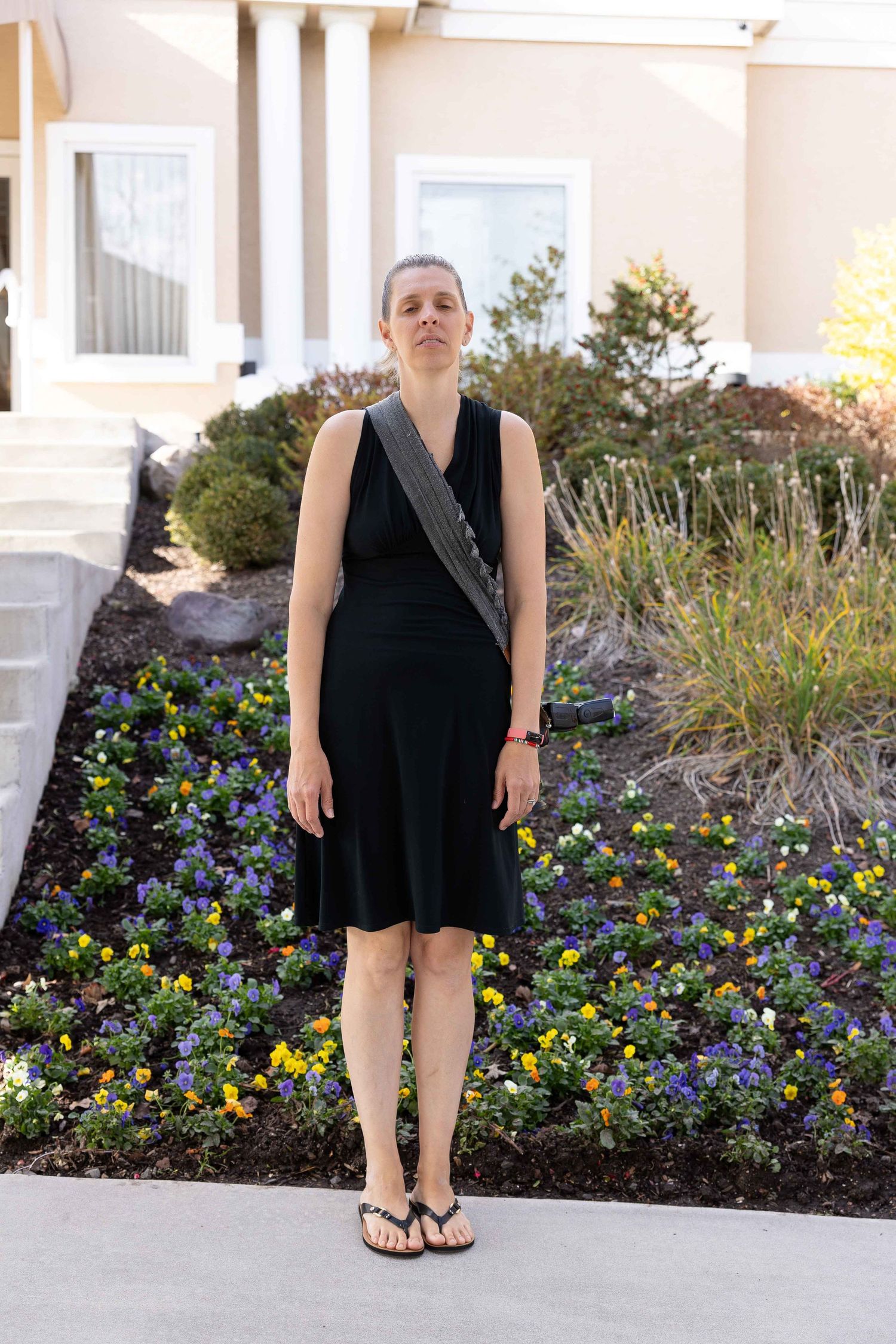 A person in a black dress stands in front of a garden bed filled with purple and yellow flowers.