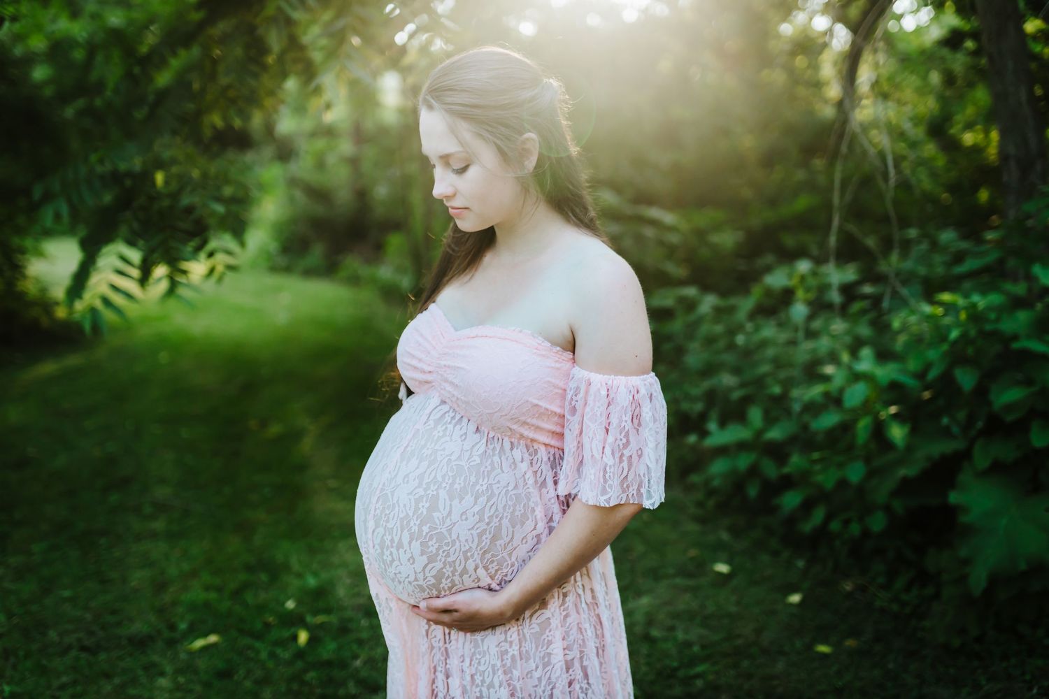 Pregnant mother wearing a pink maternity gown looks down at her belly.