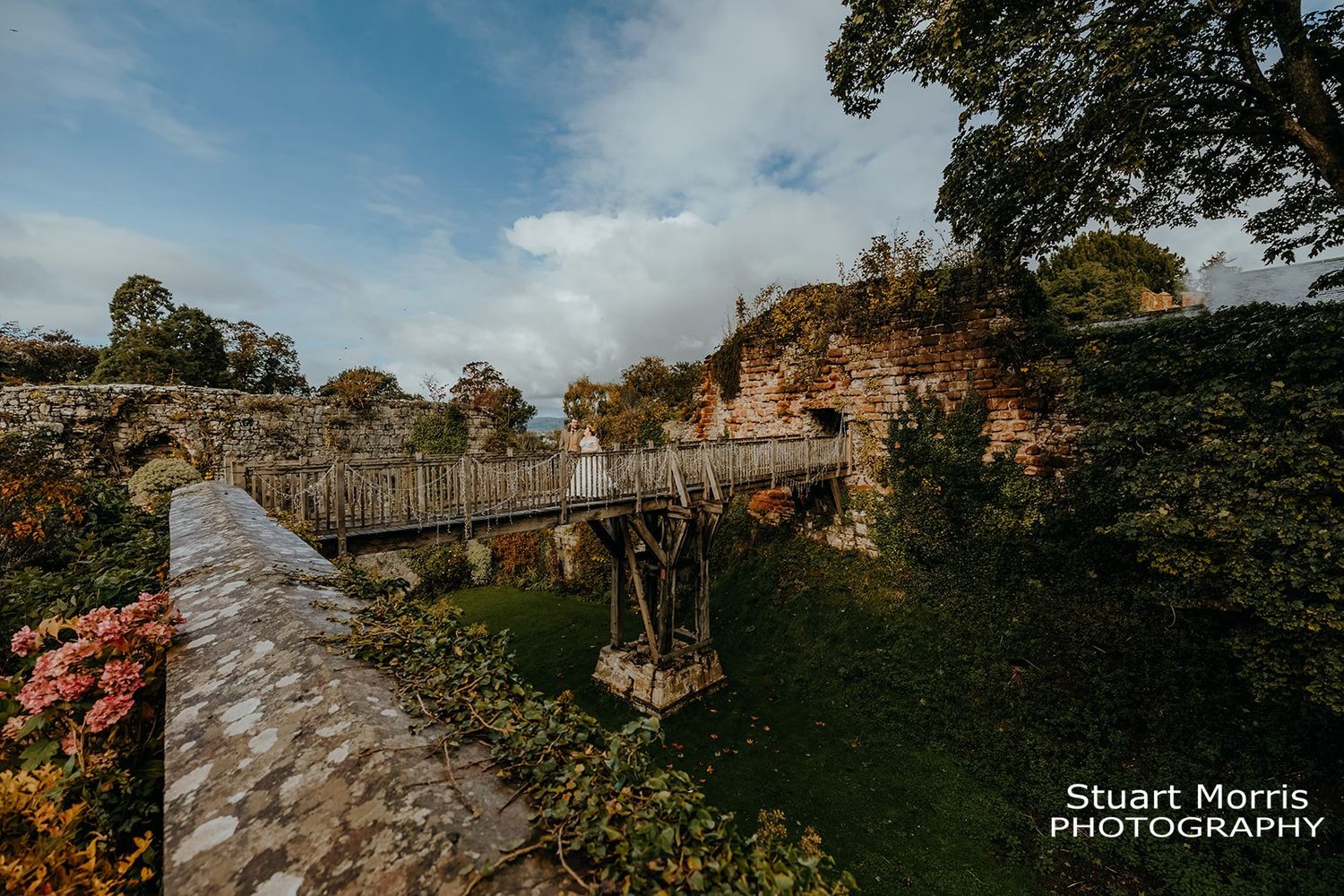 bride and groom walk across a rustic wooden bridge at Ruthin castle. north Wales wedding photographer