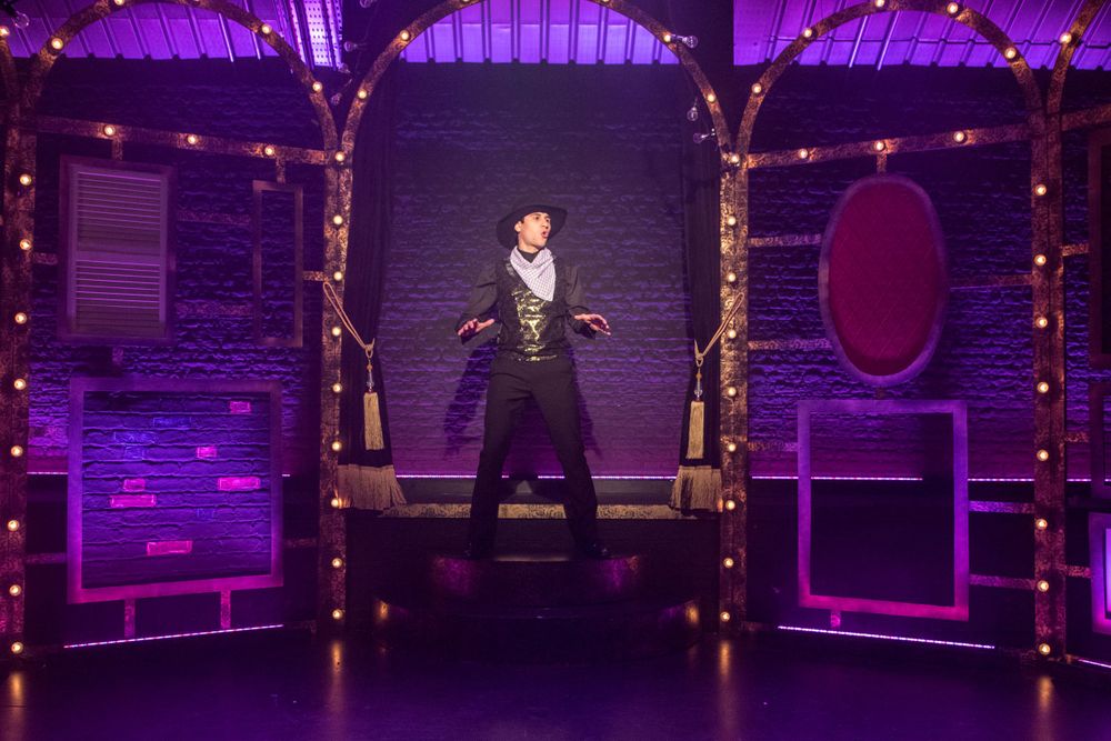 A dramatic stage performance featuring illuminated purple archways and string lights in a theatrical setting.