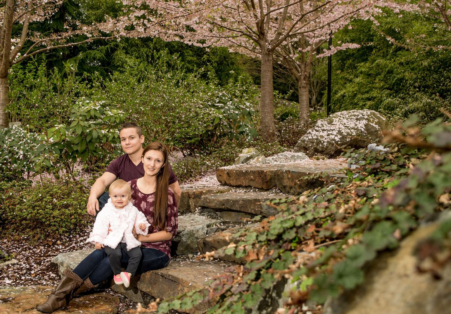 Family portrait under blooming cherry blossom trees in garden setting.