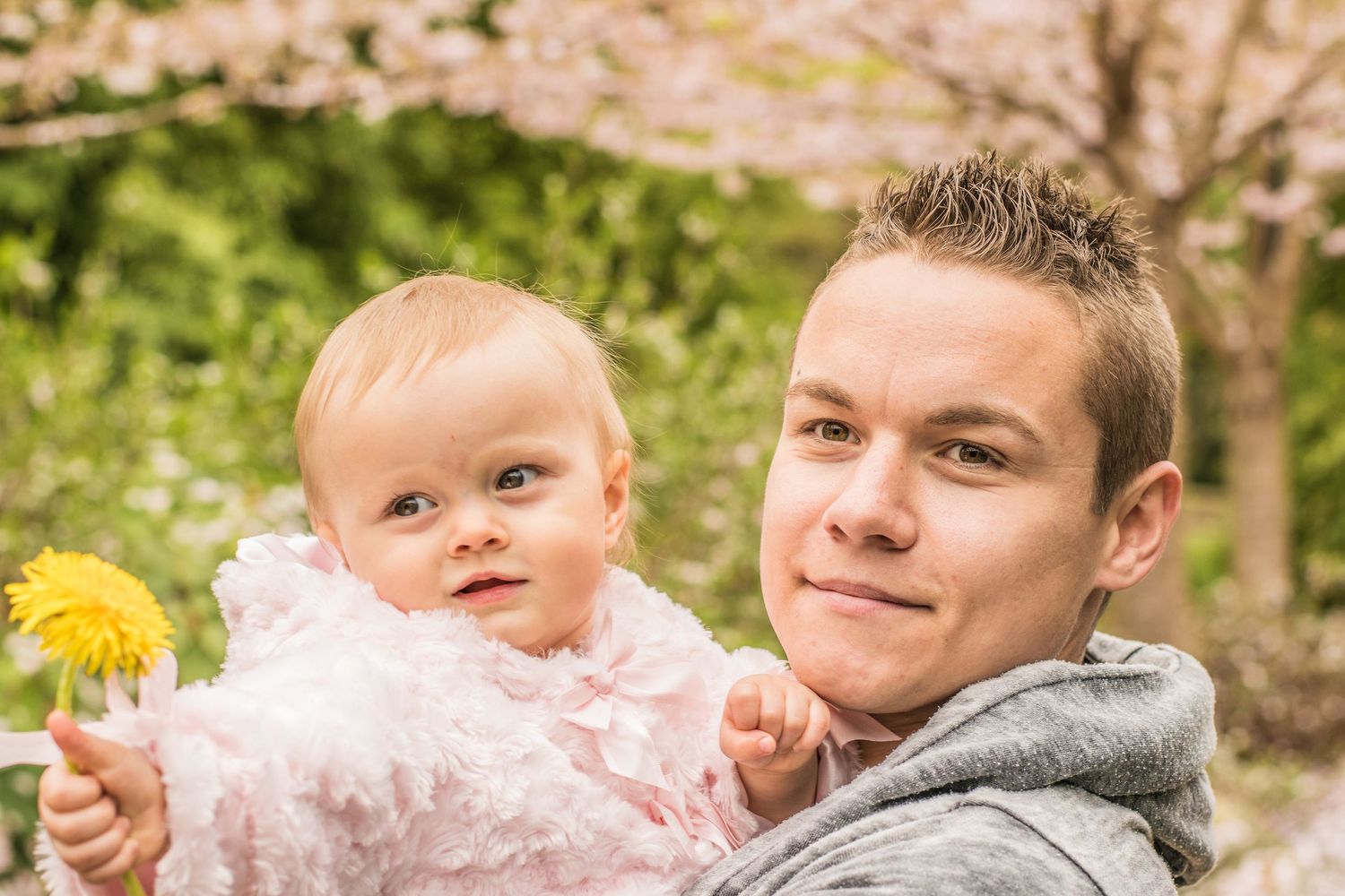 Portrait of father and baby in pink outfit under blooming cherry trees.