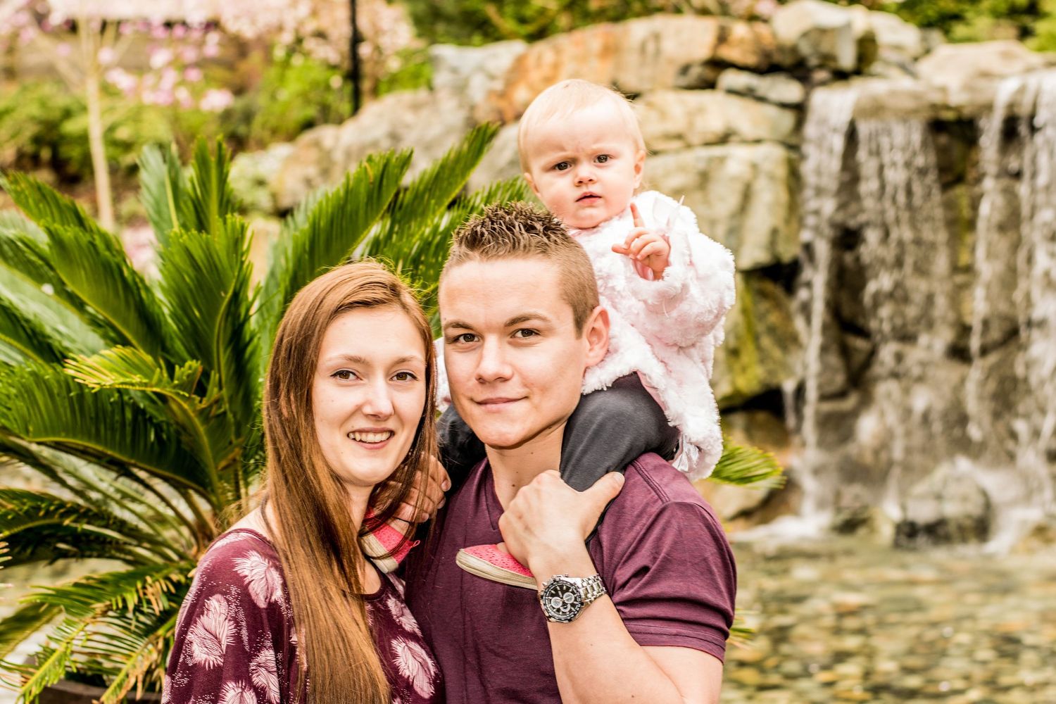 Family portrait near a waterfall with palm plants in the background.