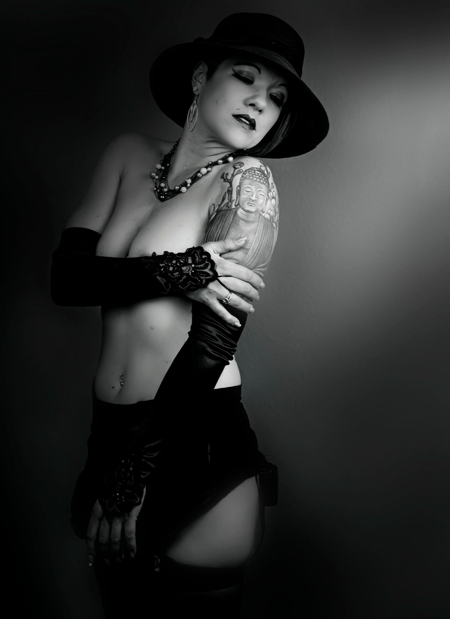 Black and white artistic boudoir photo featuring film noir styling with vintage hat, gloves and dramatic lighting.