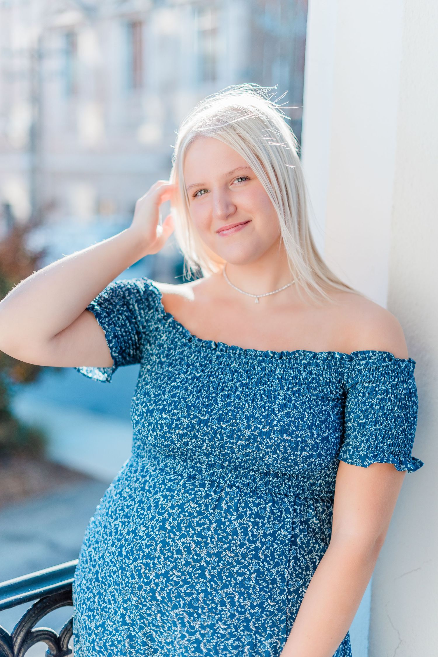 Portrait of a person in a blue floral off-shoulder dress posing outdoors on a sunny day.