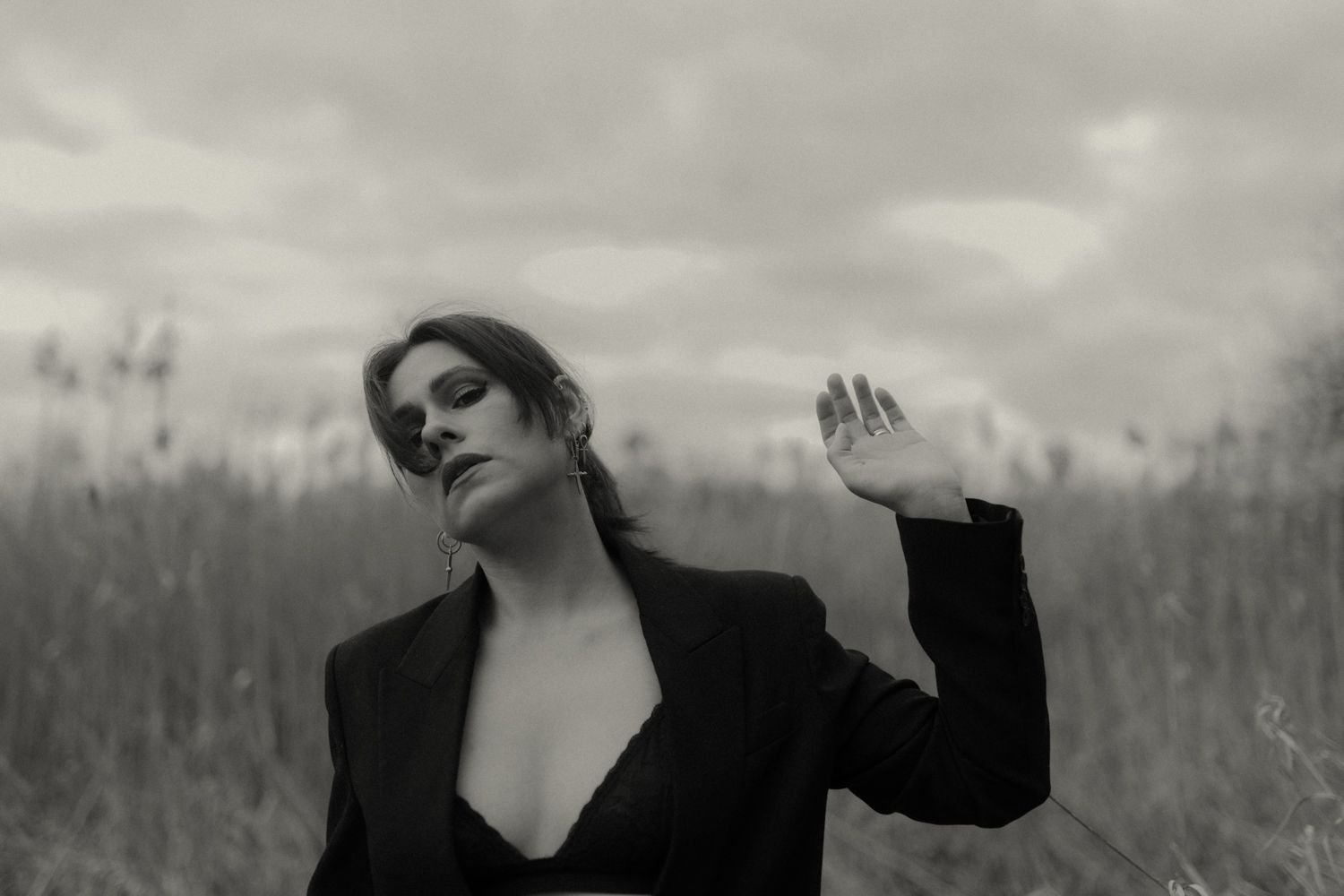 Artistic black and white portrait in tall grass under cloudy sky.