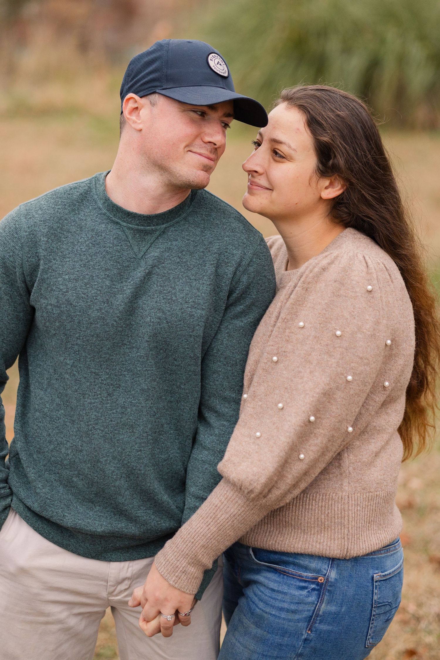 A couple in sweaters sharing an intimate moment outdoors with fall foliage in the background.