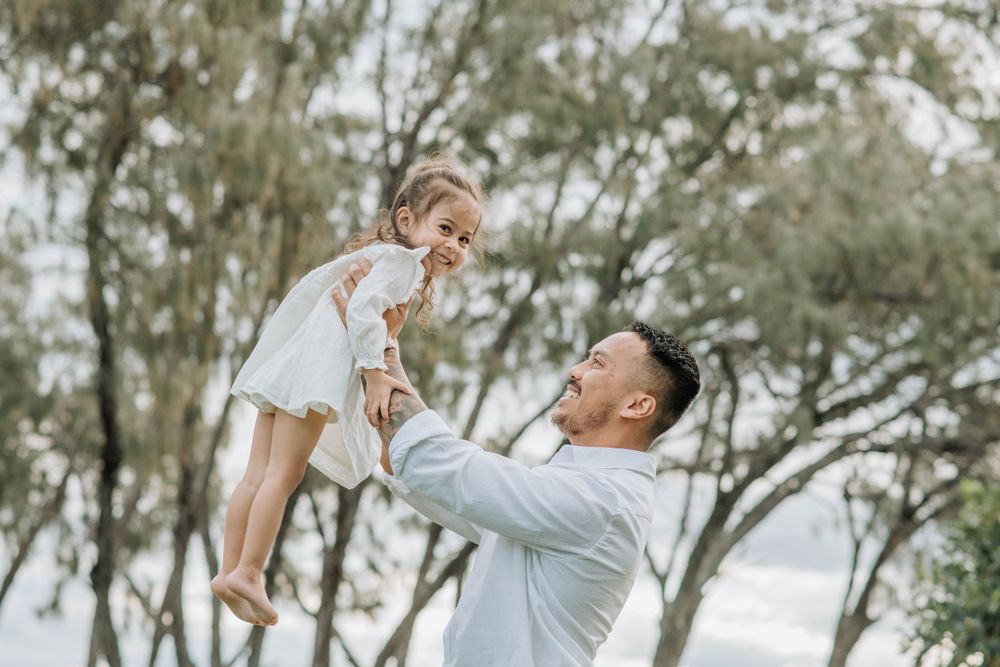 A joyful moment captured in nature as a parent lifts a small child high in the air among trees.