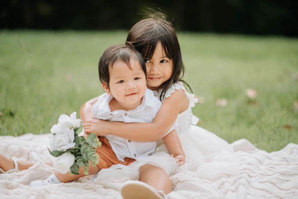 Two figures in white dresses share an embrace while sitting on a blanket outdoors.