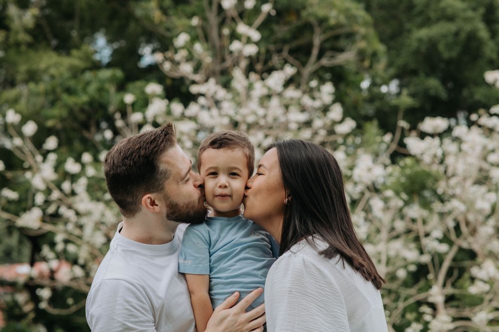 Loving parents kissing their toddler son against blooming spring trees.