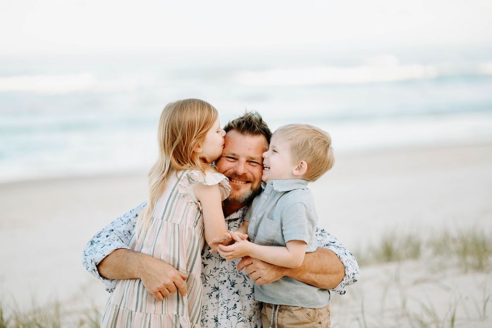 A heartwarming family moment of affection and laughter at the beach with gentle waves in the background.
