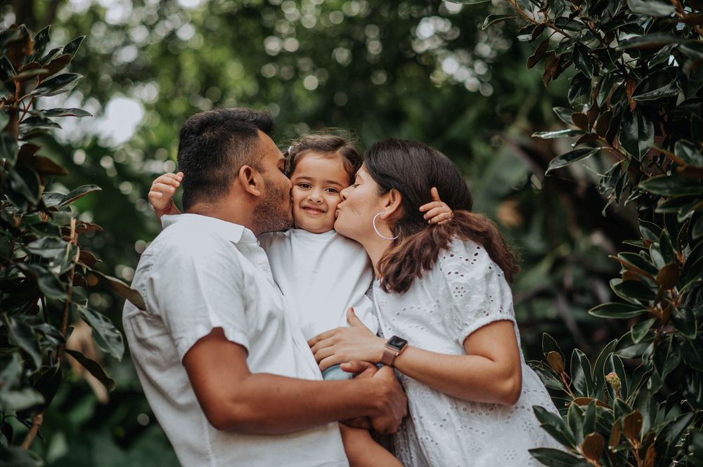 A loving family moment captured in an outdoor garden setting with white attire.