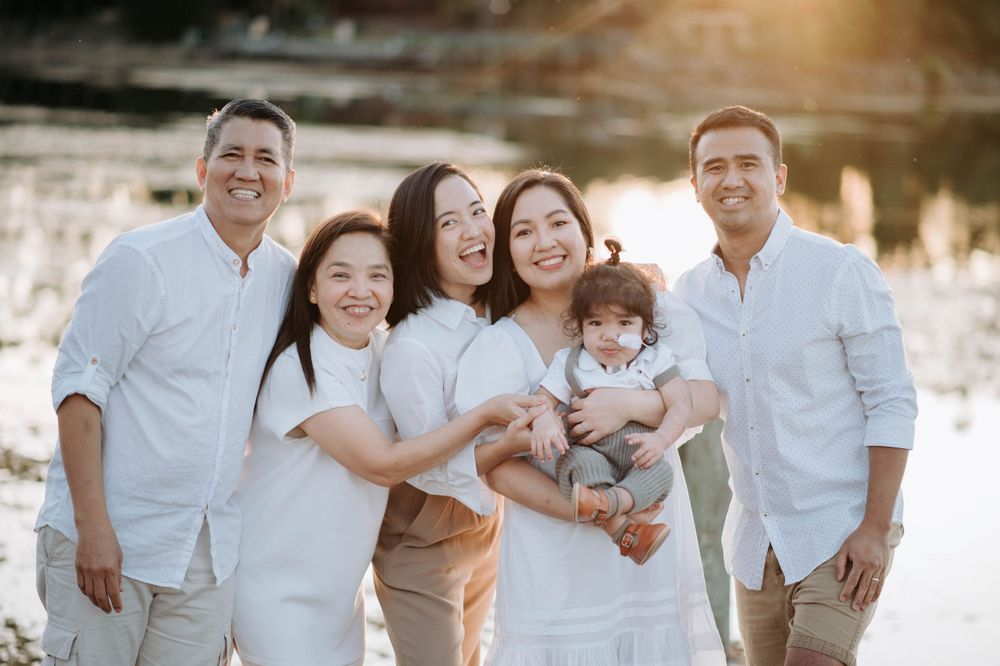 Happy family group in white clothing posing together by sunset lake.