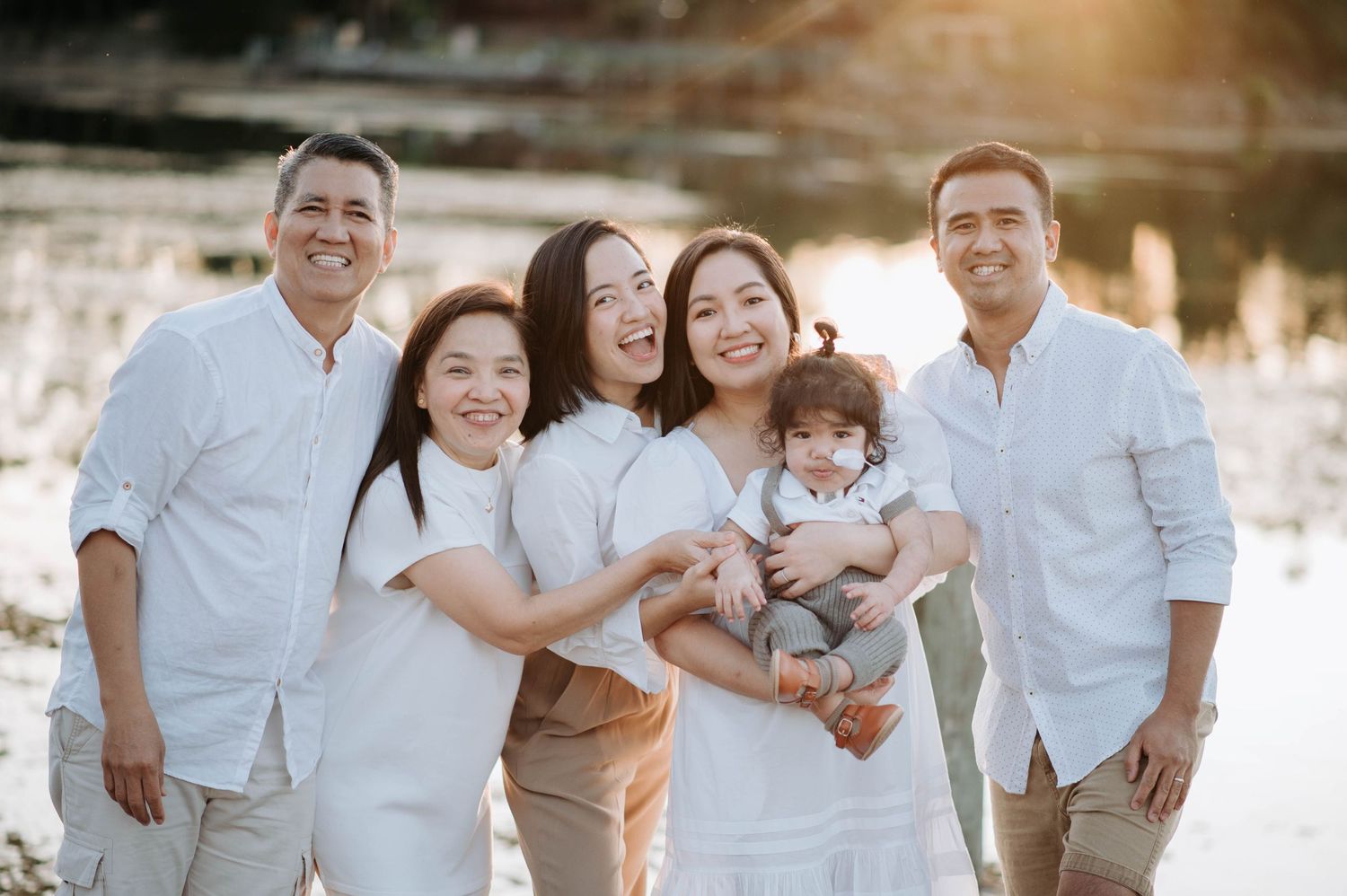Happy family group in white clothing posing together by sunset lake.