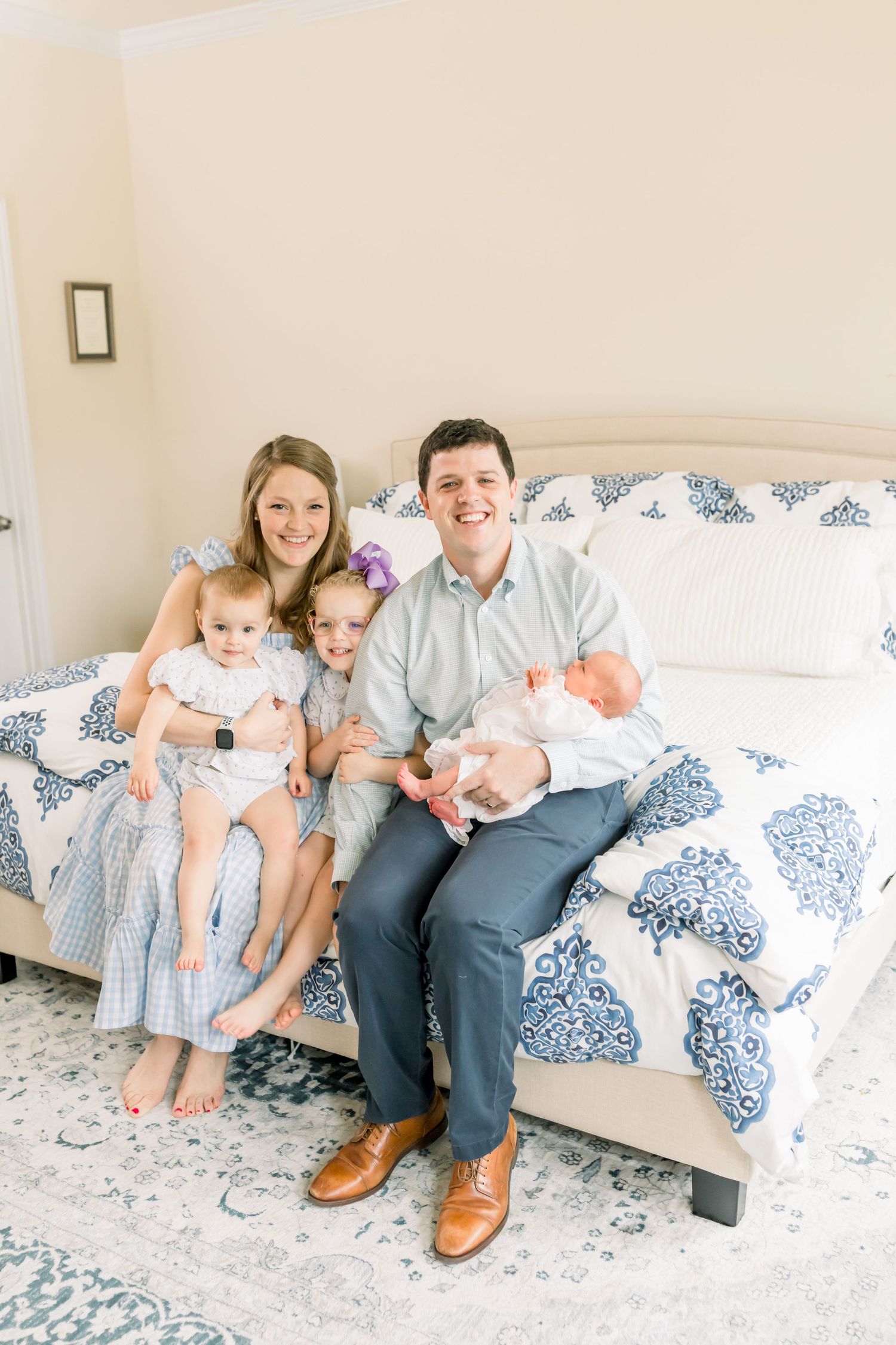 Family sitting together on a blue and white patterned bedspread in a bright bedroom.