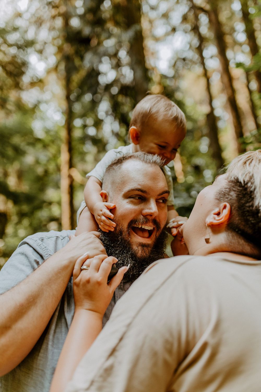 Two people share a joyful, candid moment while standing among sunlit trees in a forest.