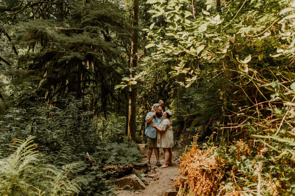 A couple walks along a scenic forest trail surrounded by lush greenery and dappled sunlight.