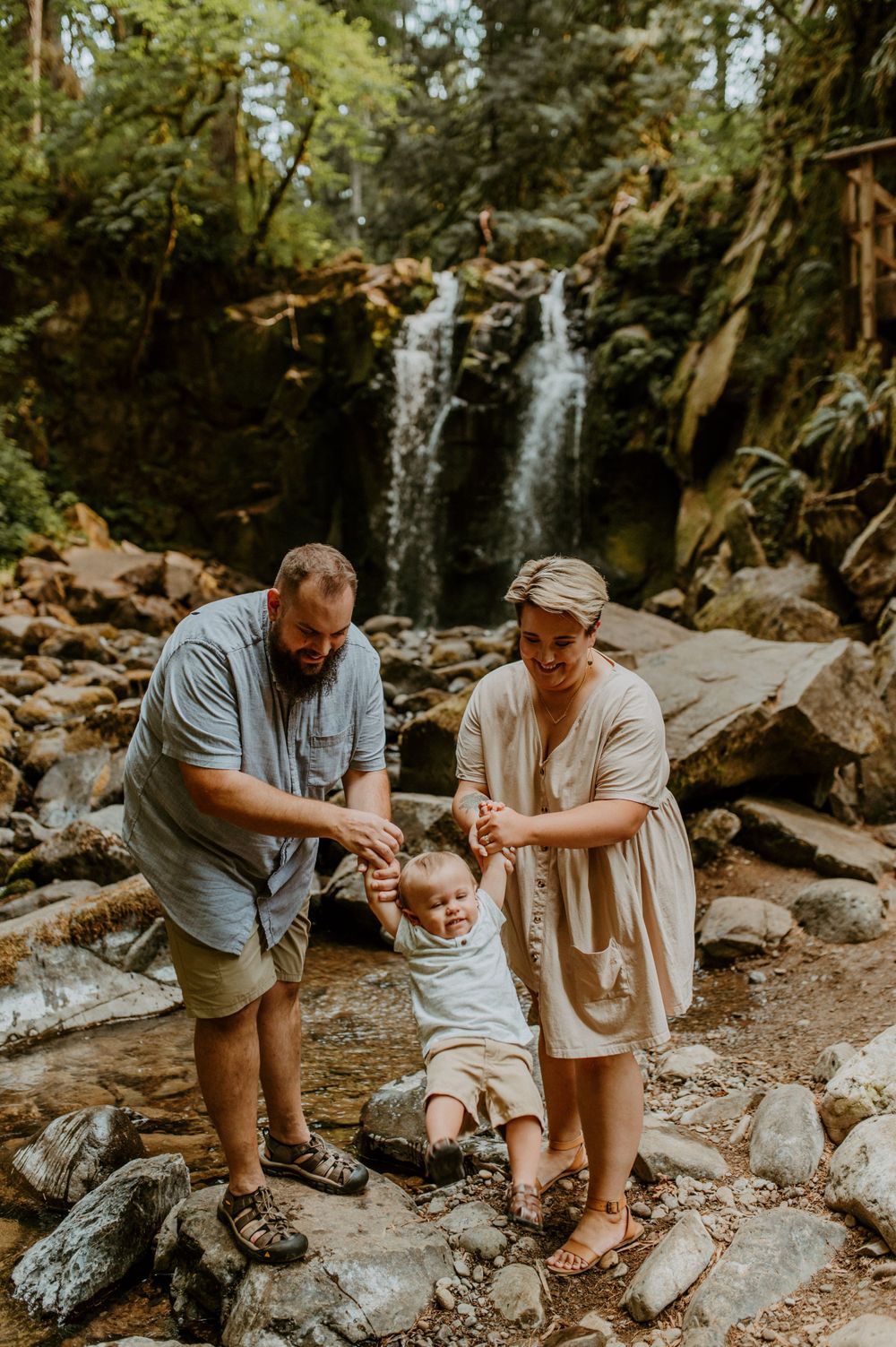 A family plays together near a scenic waterfall surrounded by rocks and forest.