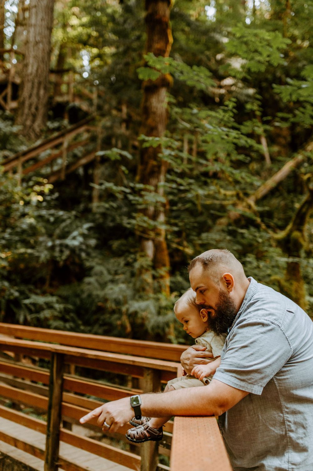 Two people share a tender moment while sitting on a wooden railing in a forested area.