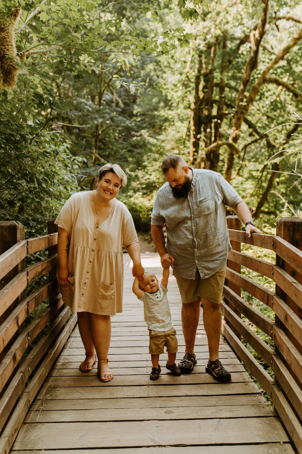 Three people walk together on a wooden boardwalk surrounded by green forest.