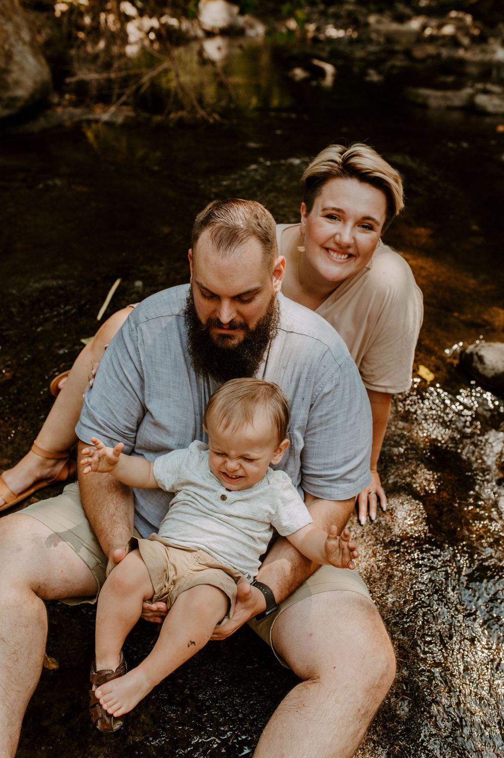 A family shares a tender moment together while sitting on rocks in a natural setting.
